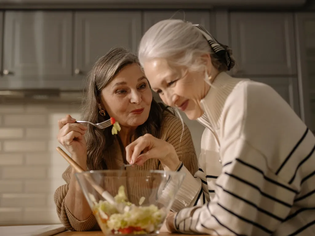 Two older women smiling over a fresh salad at home